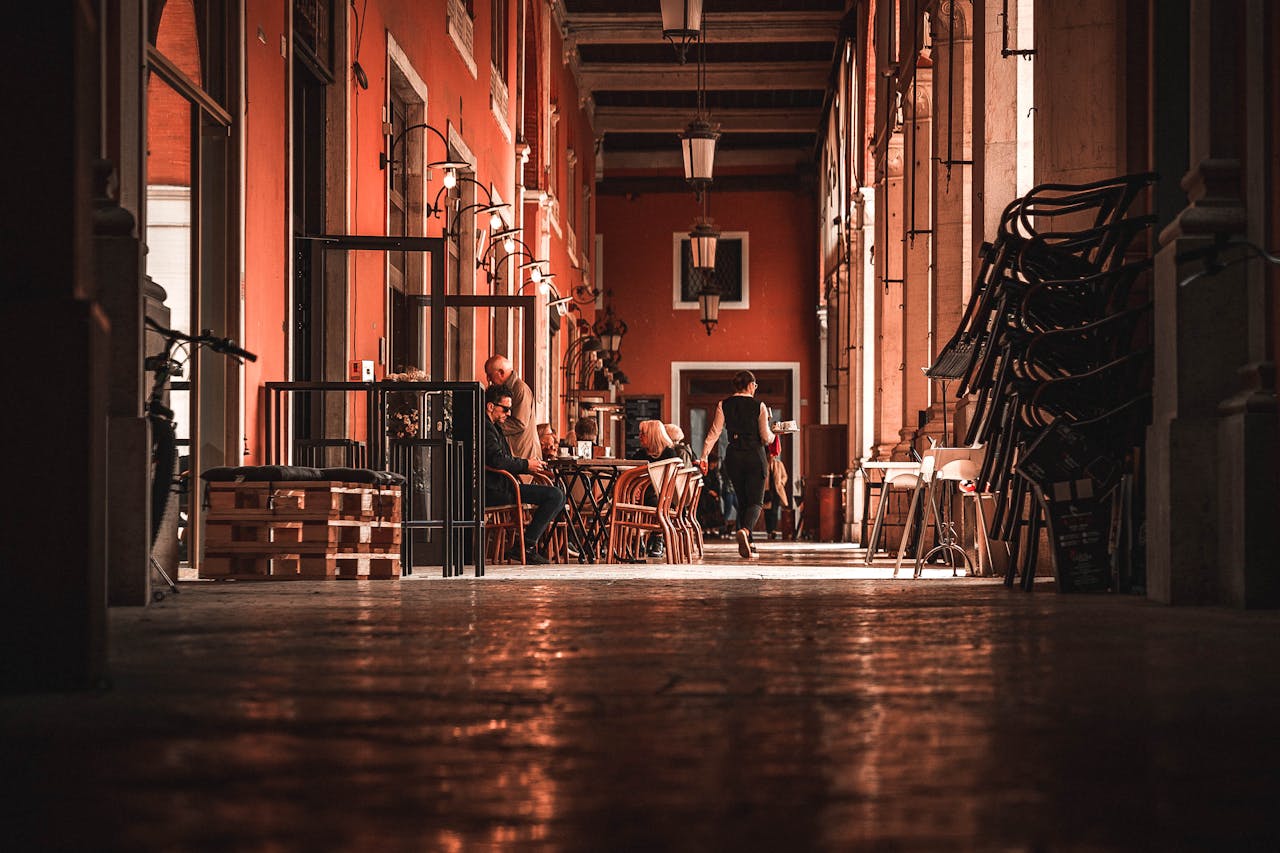 Customers enjoy drinks at an outdoor cafe in a charming urban courtyard with warm red walls.